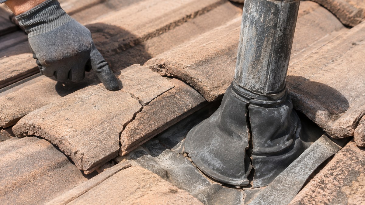 Close-up of cracked concrete roof tile and a deteriorated pipe vent boot