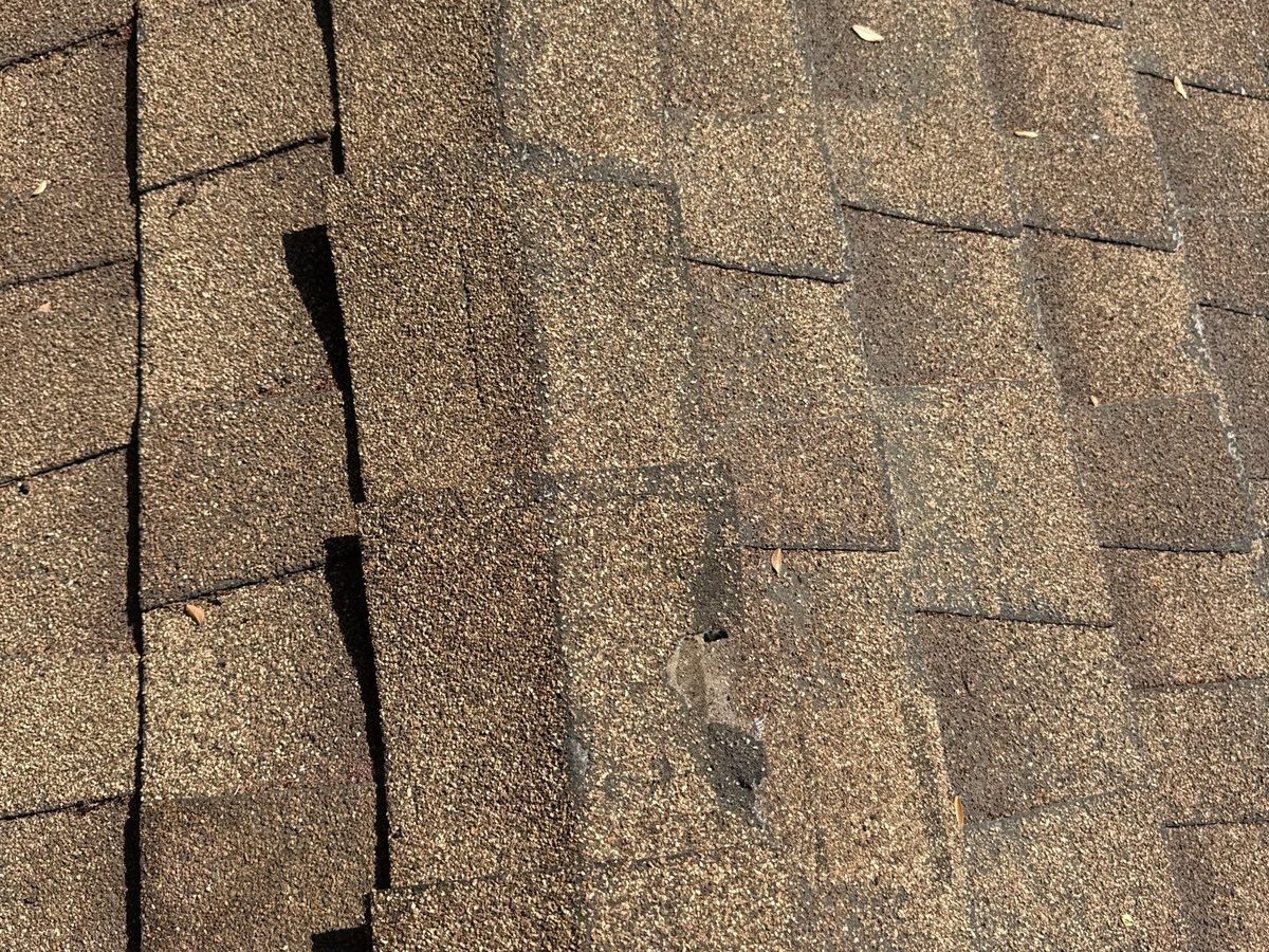 Close-up of a hip ridge on a brown asphalt shingle roof in Clovis showing ridge caps split along the fold and a piece broken out