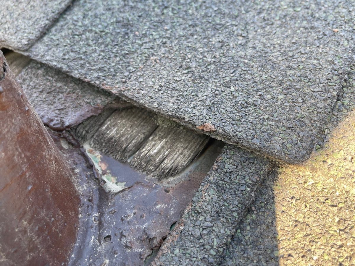 Gray shingle lifted near a plumbing vent on a Kerman roof, showing old wood shake shingles underneath